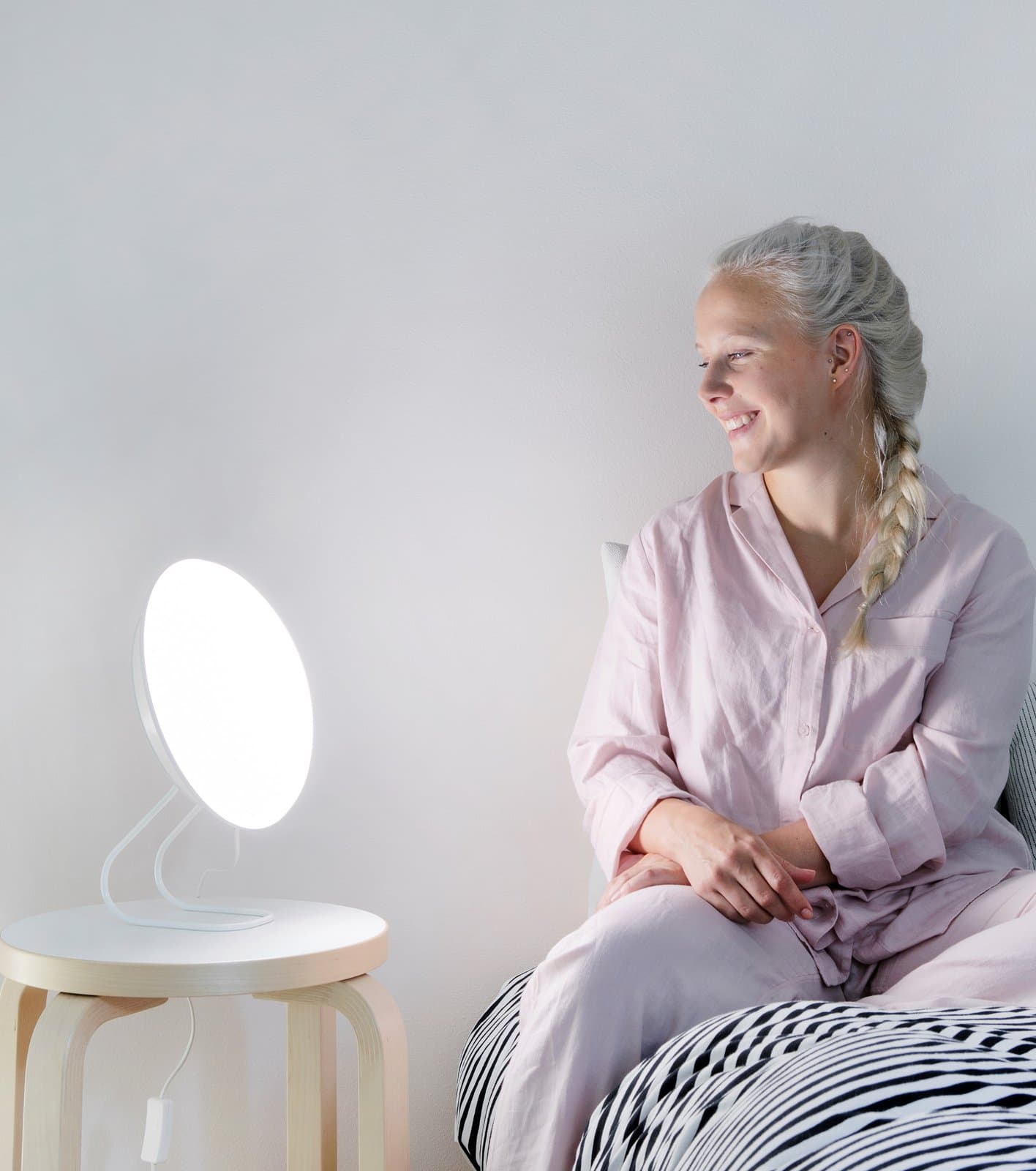 Frau im Pyjama sitzt auf dem Bett neben der eingeschalteten SAN Rondo LED